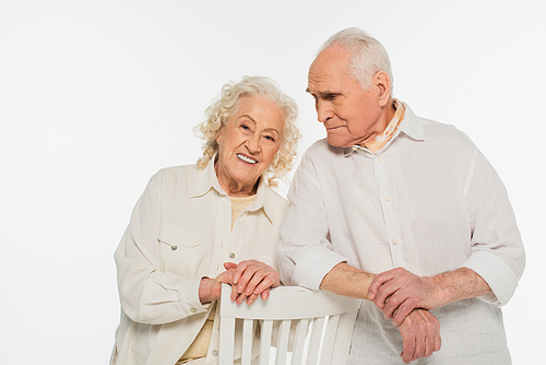 happy elderly couple in casual clothes standing near stool isolated on white