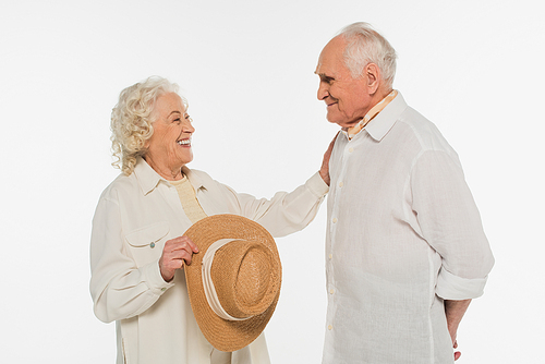 smiling elderly woman holding hat and touching husband with outstretched hand isolated on white
