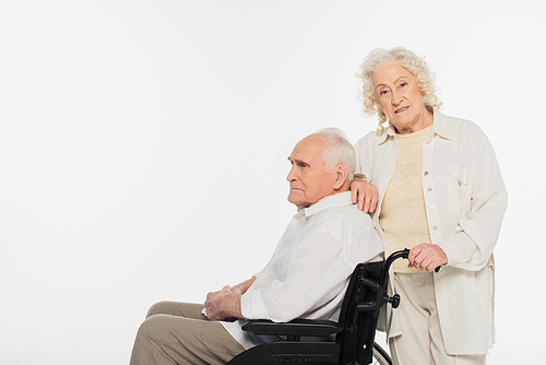 elderly woman standing near husband in wheelchair isolated on white