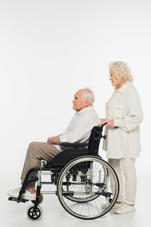 side view of elderly woman rolling husband in wheelchair on white