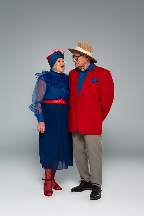 smiling elderly couple in stylish clothes standing on grey