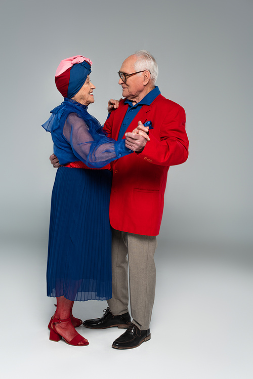 happy elderly couple in stylish clothes dancing on grey