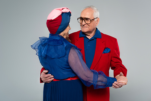 positive elderly couple in blue dress and red blazer dancing isolated on grey