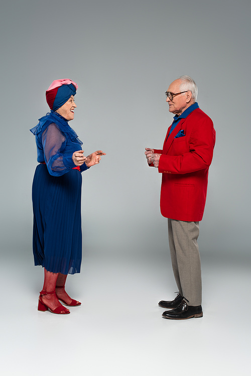 smiling elderly couple in blue dress and red blazer dancing on grey