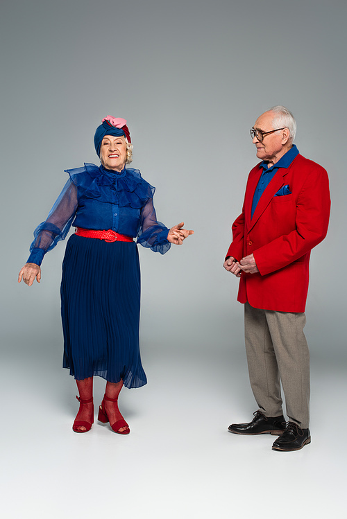 smiling elderly couple in blue dress and red blazer dancing on grey