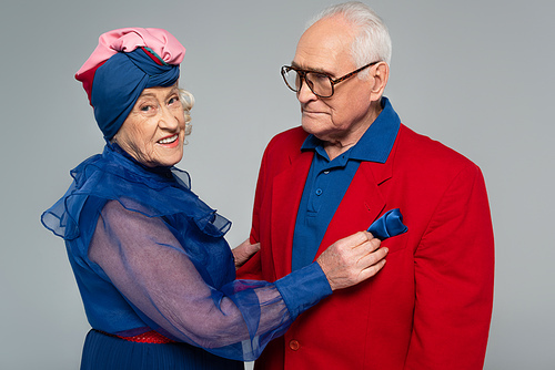 happy elderly couple in blue dress and red blazer hugging isolated on grey