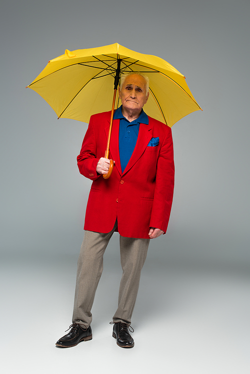 senior man in stylish clothes standing with yellow umbrella on grey