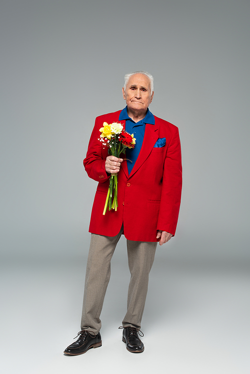 senior man in stylish clothes standing with bouquet of flowers on grey