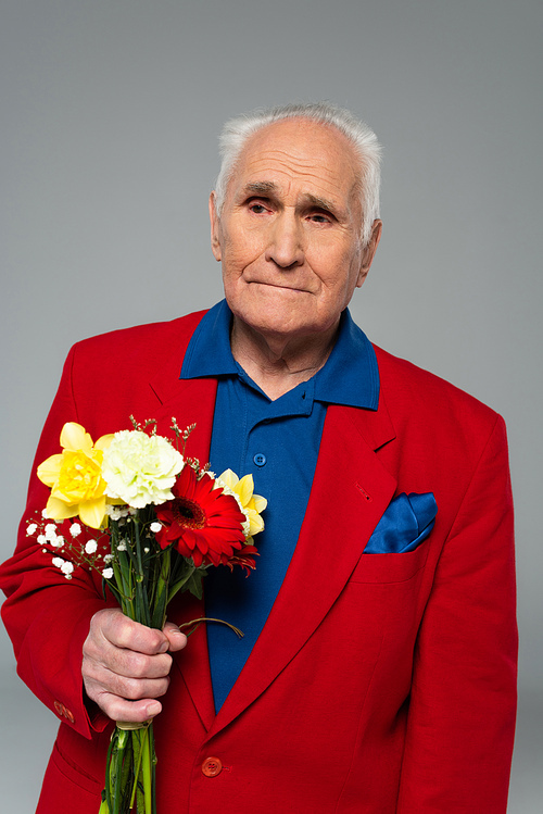 elderly man in stylish clothes standing with bouquet of flowers isolated on grey