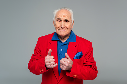 senior man in red blazer standing thumbs up gestures isolated on grey