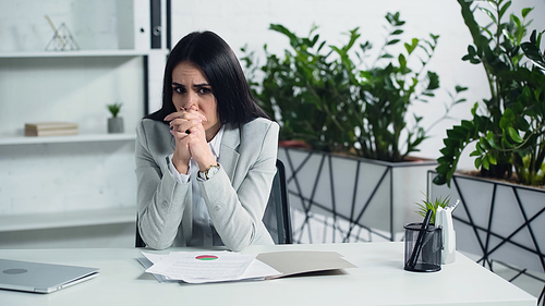 worried businesswoman sitting with clenched hands near documents in office