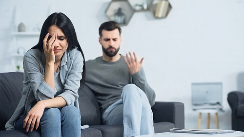 upset woman crying near blurred and displeased boyfriend quarrelling at home