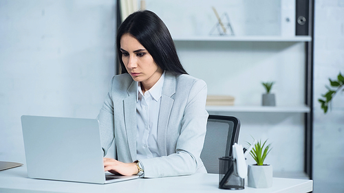 brunette and worried businesswoman using laptop in office
