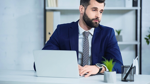 upset businessman in suit looking away near laptop on desk