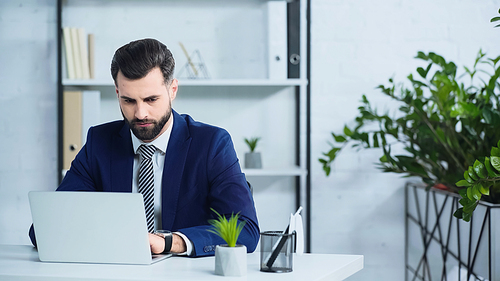 upset businessman in suit using laptop in modern office