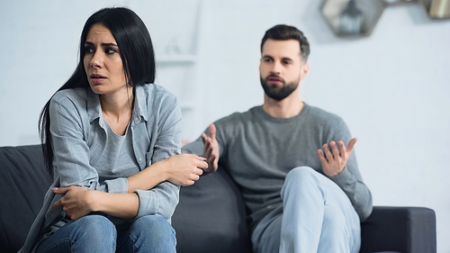 frustrated woman sitting near blurred and displeased boyfriend quarrelling in living room