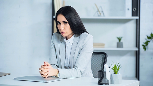 worried woman with clenched hands near laptop on desk