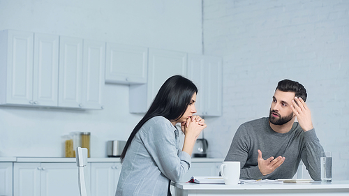 man gesturing while discussing finances with woman in kitchen