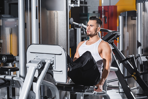 Sportsman in sportswear training on leg press machine near sports equipment in gym