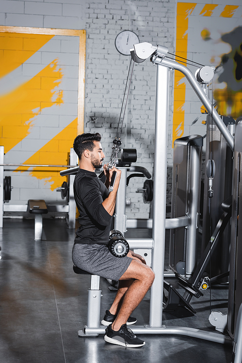 Side view of arabian man training with lat pulldown machine in gym