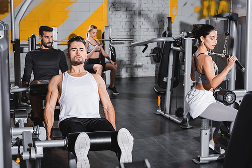 Sportsman training on leg curl machine near middle east sportswoman and sport equipment in gym