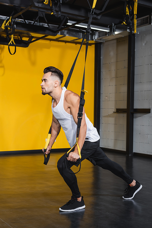 Young sportsman training with suspension straps in sports center