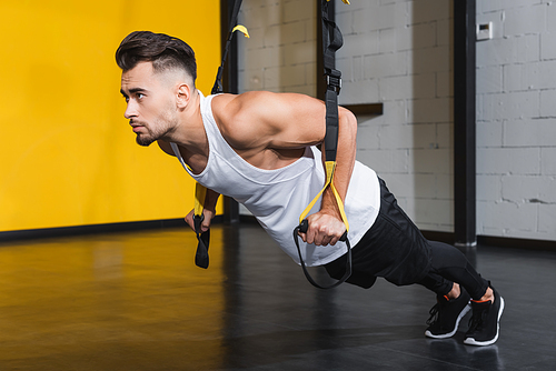 Young sportsman training with suspension straps in sports center