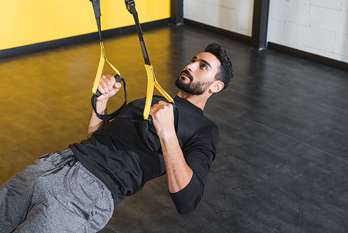 Bearded muslim sportsman training with suspension straps in gym