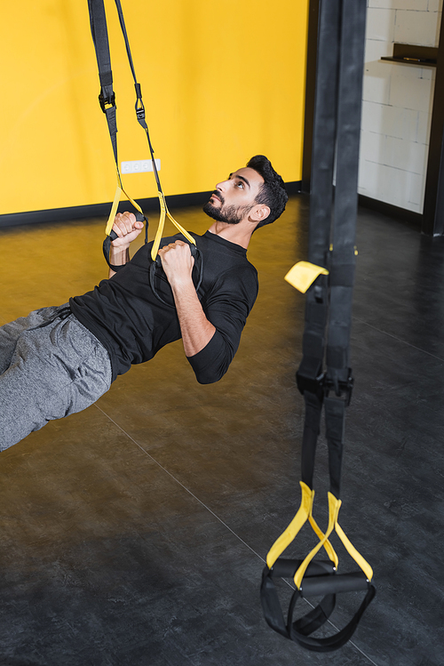 Muslim sportsman training with suspension straps in gym