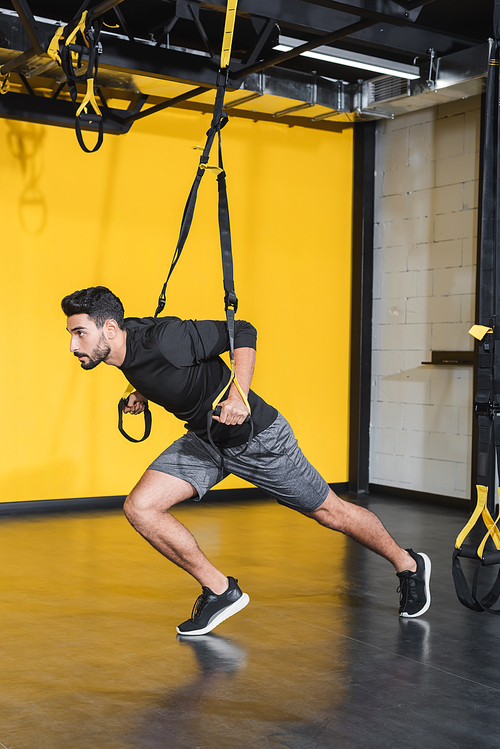 Athletic arabian sportsman training with suspension straps in sports center