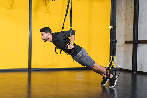 Side view of muslim sportsman working out with suspension straps in sports center