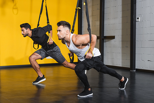 Athletic interracial sportsmen training with suspension straps in sports center