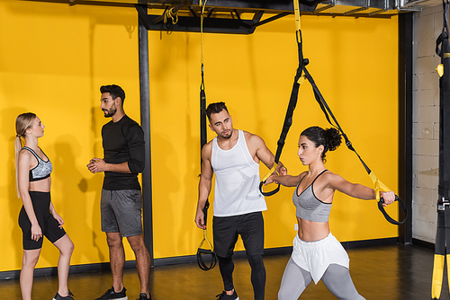 Middle east sportswoman pulling suspension straps near friends in gym