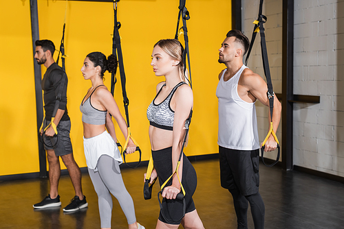 Sportswoman pulling suspension straps while training with interracial friends in sports center