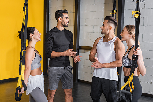 Smiling interracial people talking near suspension straps in gym