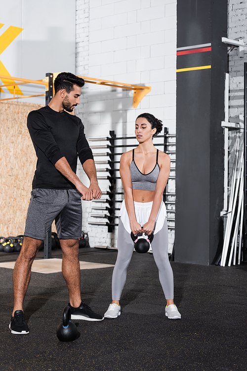 Arabian trainer standing near middle east sportswoman training with kettlebell in gym