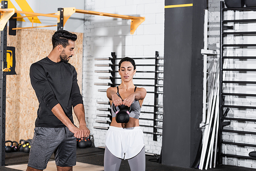 Middle east sportswoman training with kettlebell near muslim trainer in sports center