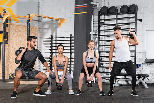 Smiling multiethnic people training with kettlebells in sports center