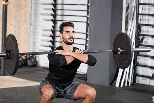 Arabian sportsman training with barbell in blurred sports center