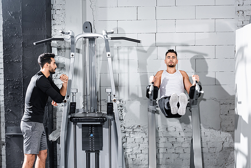 Sportsman training on parallel bar near arabian trainer in gym