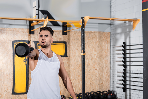 Athletic sportsman working out with kettlebell in blurred gym