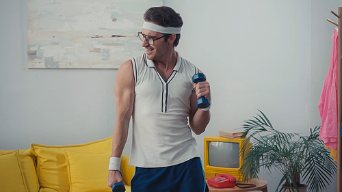 funny sportsman exercising with dumbbells in living room, retro sport concept