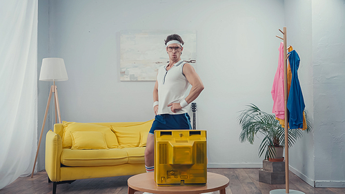 funny sportsman with hands on hips exercising in front of retro tv at home