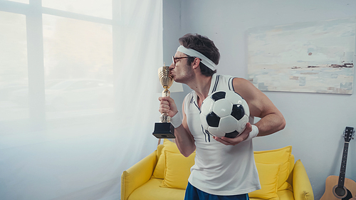 football player kissing golden trophy cup and holding soccer ball