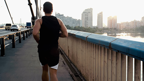 back view of athletic mixed race man running on city bridge over river