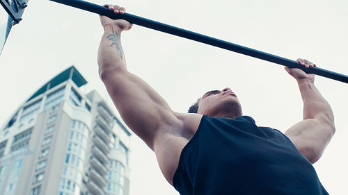 low angle view of tattooed mixed race man working out on horizontal bar outdoors