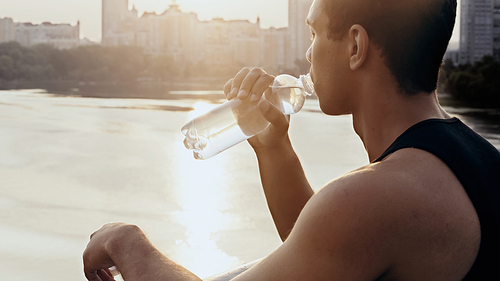 young bi-racial man drinking water over river at dawn