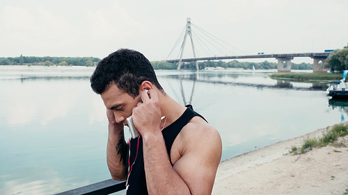 athletic bi-racial man adjusting earphones while standing near river