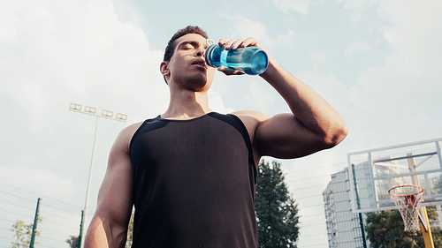 low angle view of bi-racial sportsman drinking water from sports bottle outdoors