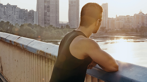 bi-racial sportive man standing on bridge over river at dawn